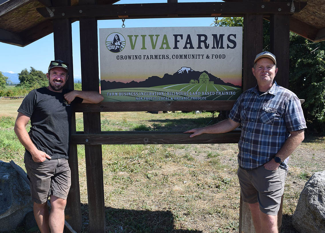 Rob Smith standing on the left, Michael Frazier standing on the right side of a Viva Farms sign